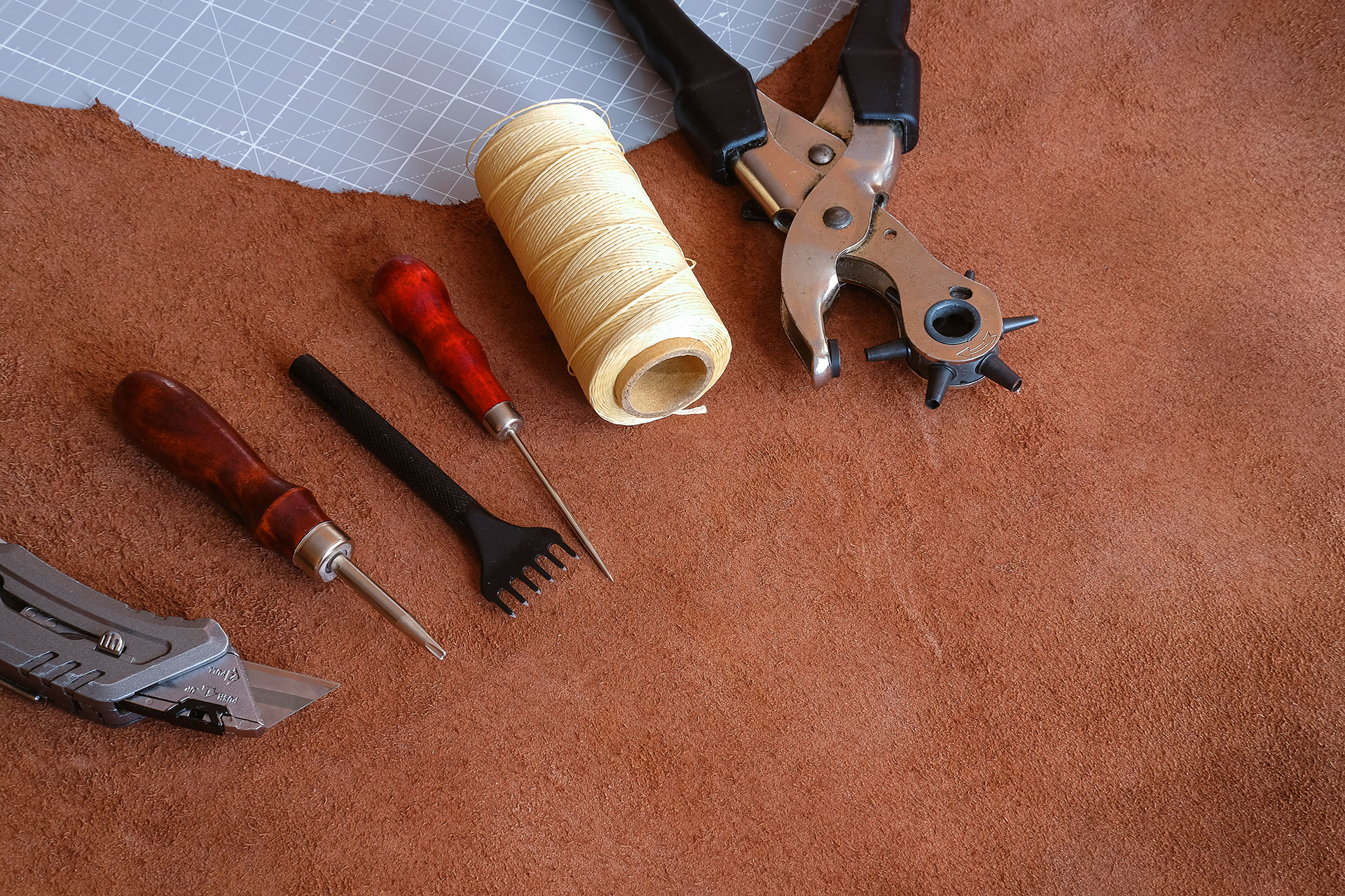 Leather crafting tools and waxed thread on suede hide