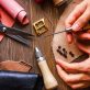 Hands stitching leather piece with awl and hardware on workbench