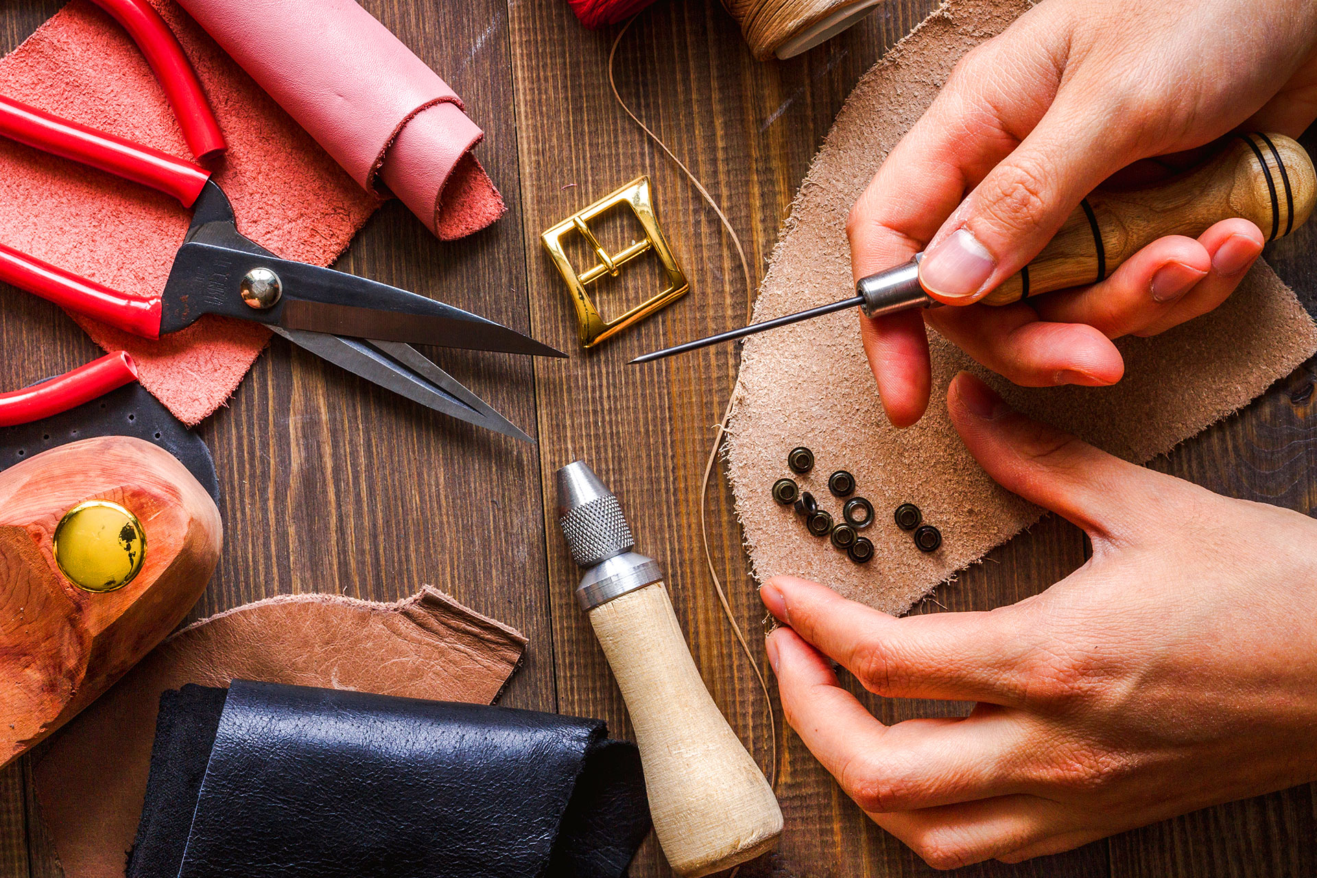 Hands stitching leather piece with awl and hardware on workbench